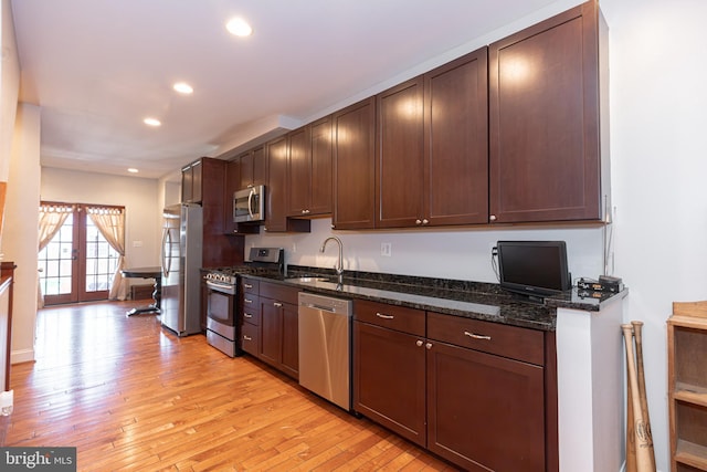 kitchen with dark stone countertops, sink, light wood-type flooring, stainless steel appliances, and french doors