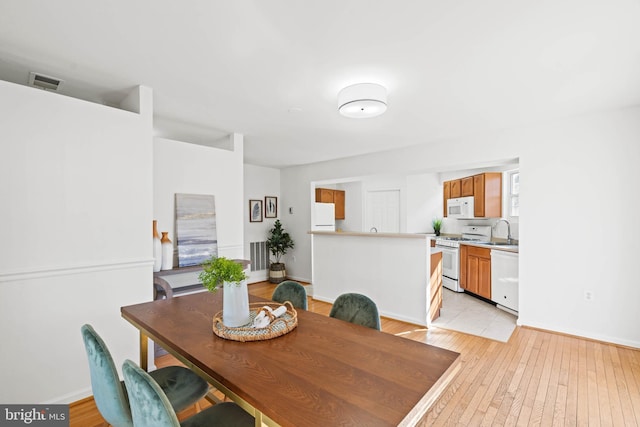 dining room with light wood-type flooring, visible vents, and baseboards