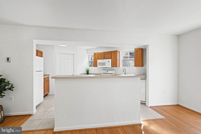 kitchen featuring white appliances, a sink, light countertops, brown cabinets, and light wood finished floors