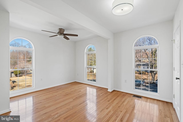 empty room featuring wood-type flooring, visible vents, ceiling fan, beamed ceiling, and baseboards