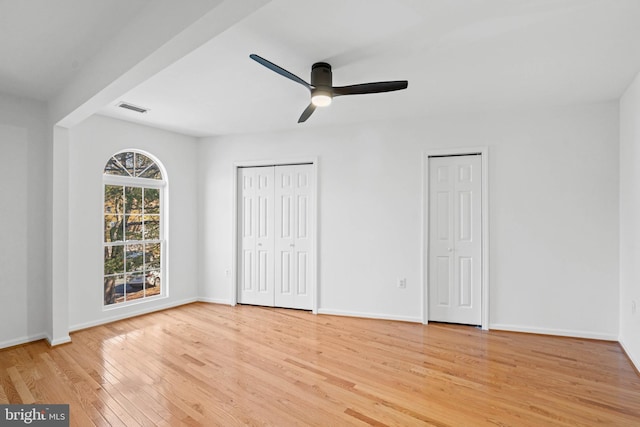 unfurnished bedroom with light wood finished floors, baseboards, visible vents, and multiple closets