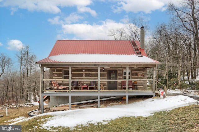 view of front facade with covered porch, metal roof, a chimney, and log siding