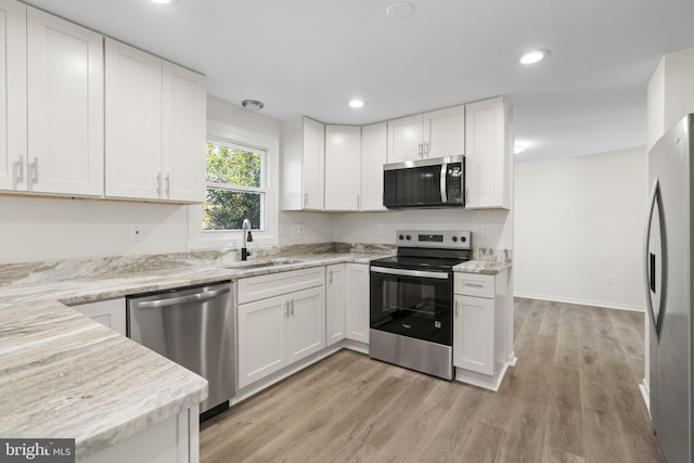 kitchen featuring appliances with stainless steel finishes, a sink, white cabinetry, and light stone countertops