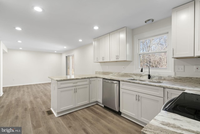 kitchen featuring light wood-style flooring, stainless steel appliances, a peninsula, a sink, and white cabinetry