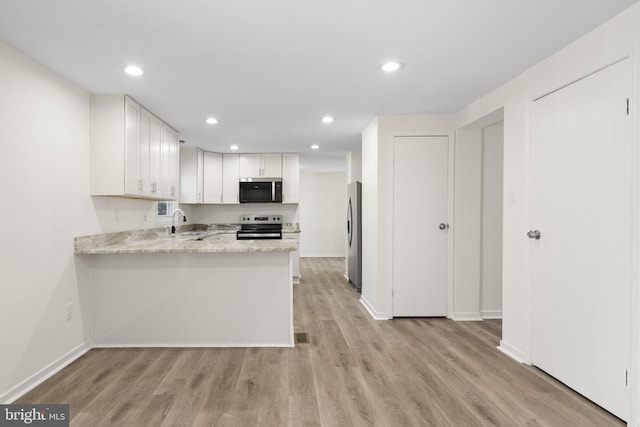 kitchen with appliances with stainless steel finishes, white cabinetry, light stone countertops, light wood-type flooring, and a peninsula