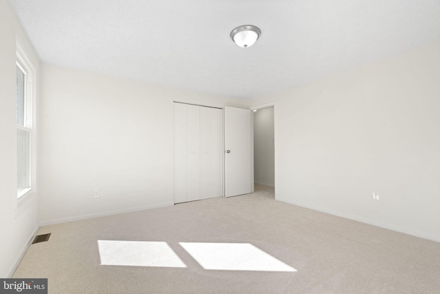 unfurnished bedroom with light colored carpet, a closet, visible vents, and baseboards