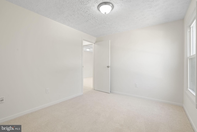 empty room featuring light carpet, a textured ceiling, and baseboards