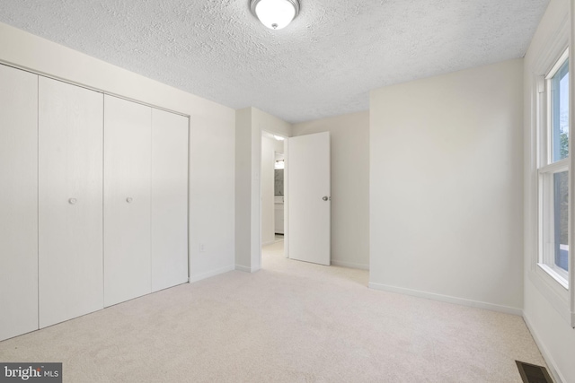 unfurnished bedroom featuring a closet, light colored carpet, visible vents, a textured ceiling, and baseboards