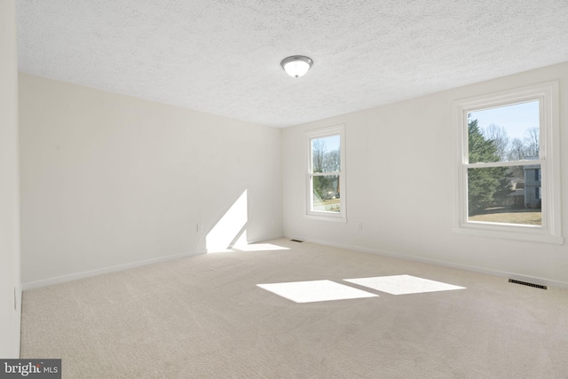 unfurnished room featuring a textured ceiling, baseboards, visible vents, and light colored carpet