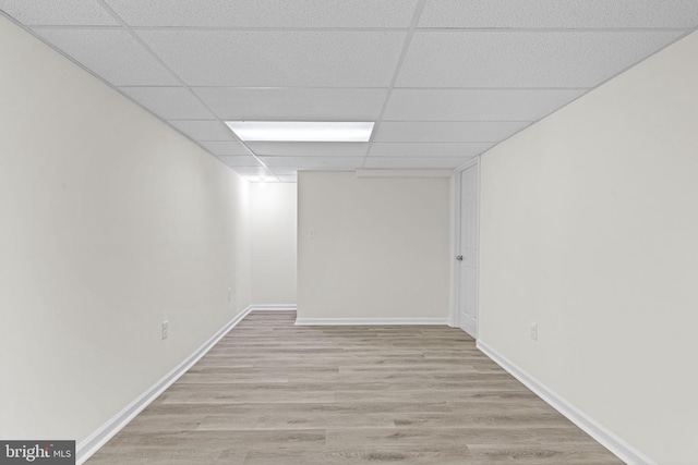 unfurnished room with light wood finished floors, a drop ceiling, and baseboards