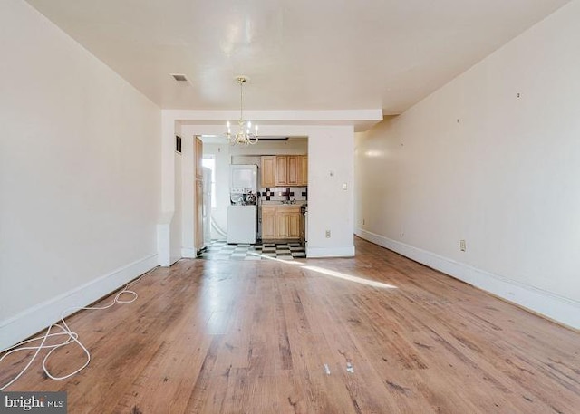 unfurnished living room featuring an inviting chandelier and light hardwood / wood-style floors