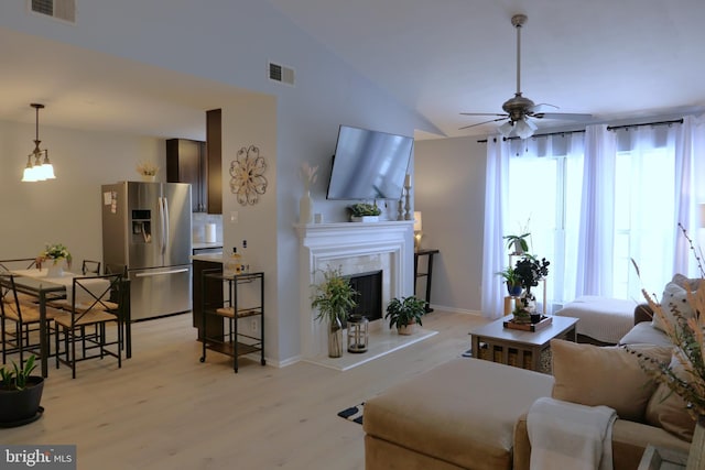 living room featuring light hardwood / wood-style flooring, a high end fireplace, vaulted ceiling, and ceiling fan