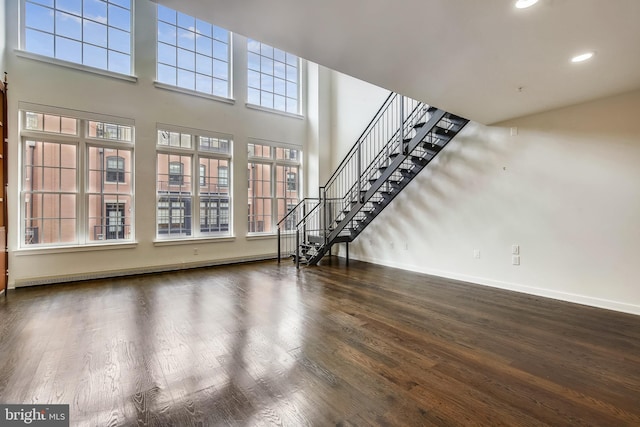 unfurnished living room featuring baseboards, wood finished floors, a high ceiling, stairs, and recessed lighting