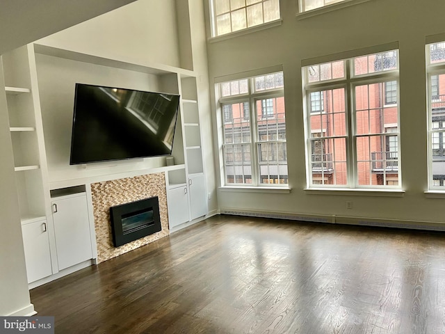 unfurnished living room with built in features, a fireplace, a towering ceiling, a baseboard heating unit, and wood finished floors