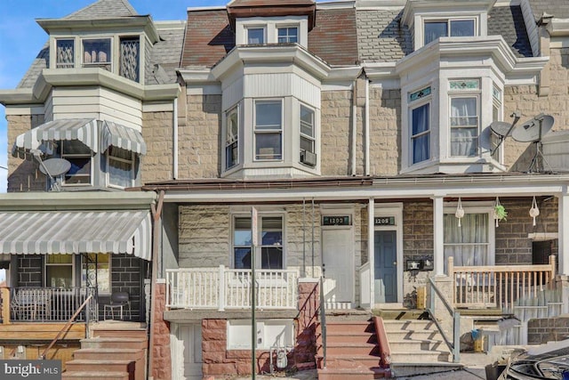 multi unit property featuring stone siding, covered porch, and mansard roof