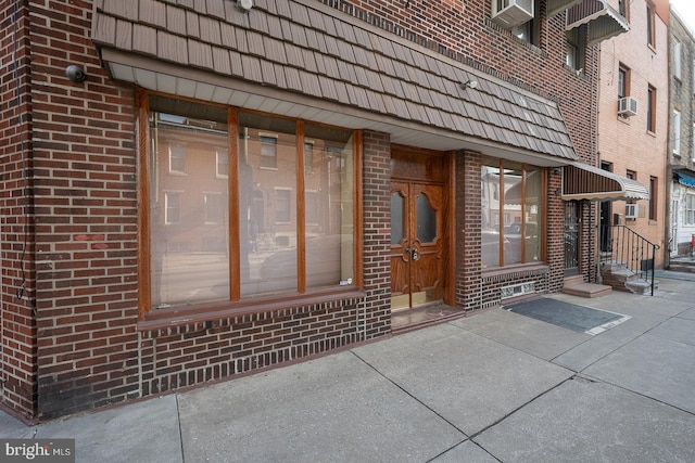 entrance to property with brick siding, mansard roof, and cooling unit