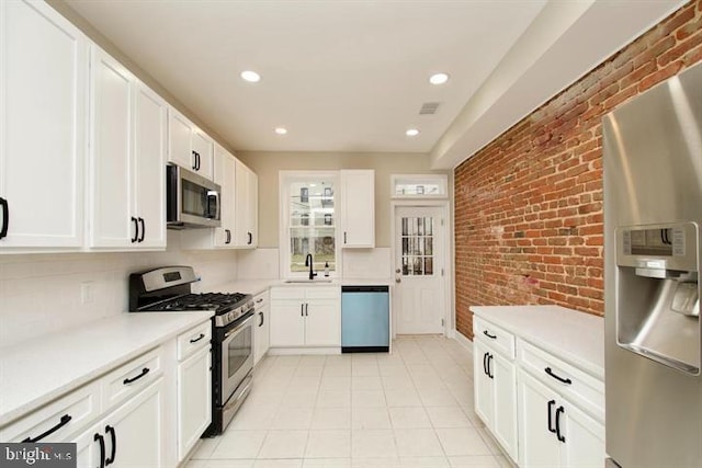 kitchen with brick wall, appliances with stainless steel finishes, white cabinetry, sink, and decorative backsplash