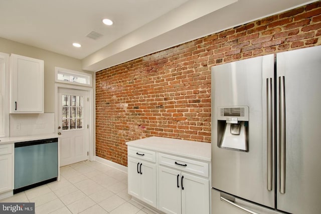 kitchen with brick wall, stainless steel appliances, light tile patterned floors, and white cabinets