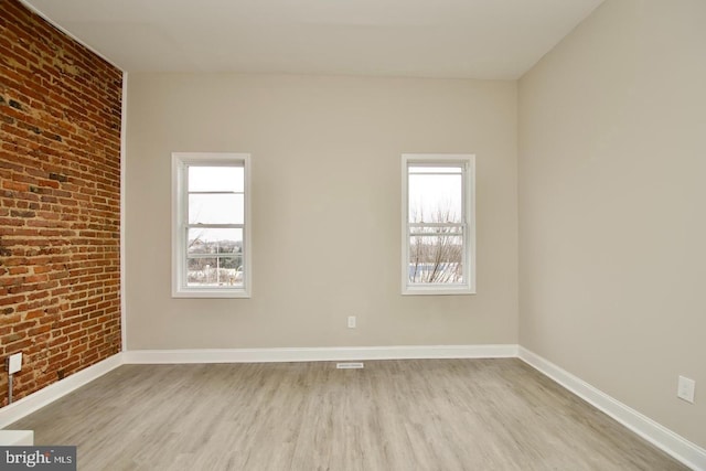 unfurnished room featuring brick wall and light hardwood / wood-style flooring