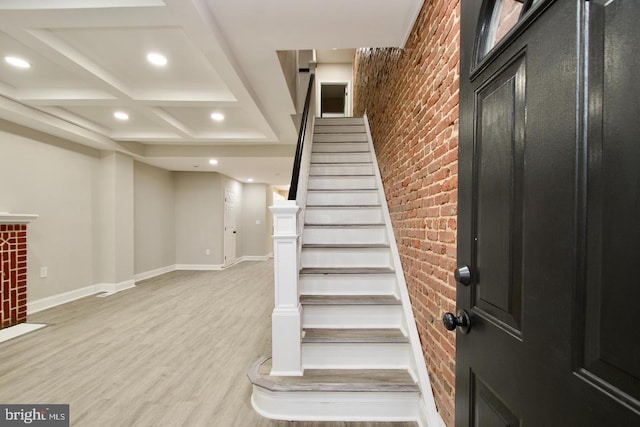 foyer with brick wall, coffered ceiling, and light hardwood / wood-style flooring