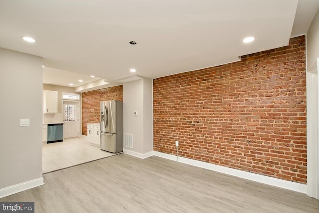 unfurnished living room featuring brick wall and light wood-type flooring