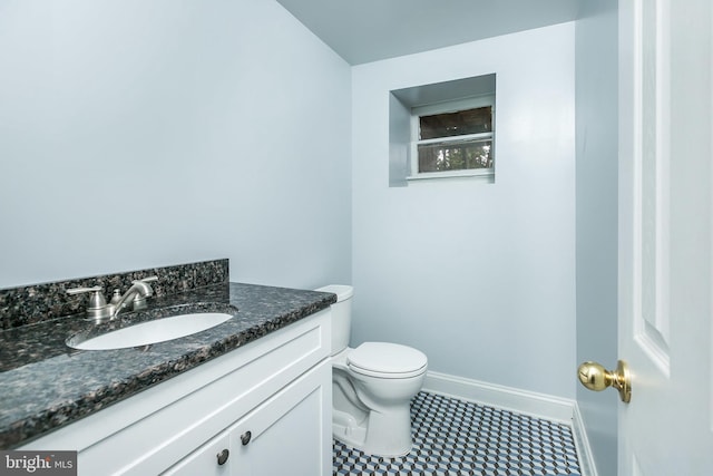 half bathroom featuring toilet, tile patterned floors, vanity, and baseboards