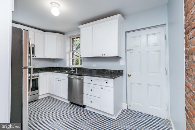 kitchen featuring brick wall, appliances with stainless steel finishes, tile patterned floors, and white cabinets