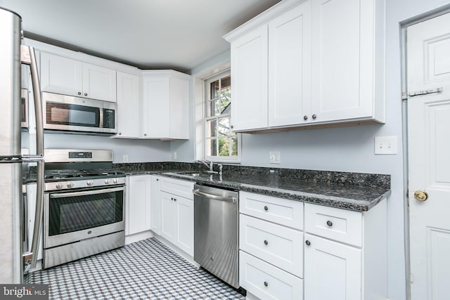 kitchen featuring appliances with stainless steel finishes, white cabinetry, a sink, and dark stone countertops