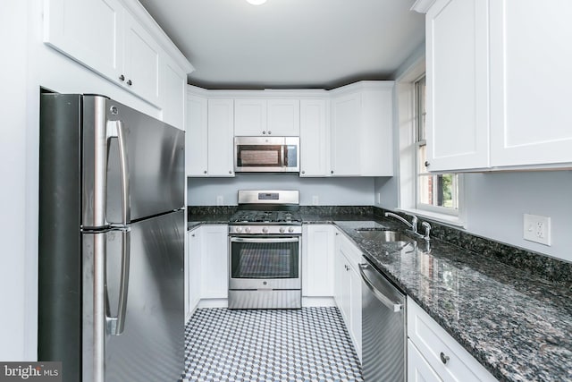 kitchen with dark stone counters, appliances with stainless steel finishes, a sink, and white cabinets