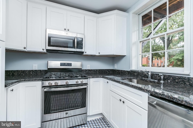 kitchen with appliances with stainless steel finishes, dark stone countertops, a sink, and white cabinetry