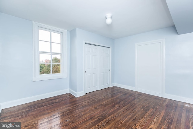 unfurnished bedroom with a closet, dark wood-style flooring, and baseboards