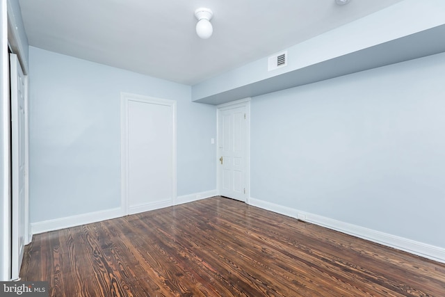 empty room with dark wood finished floors, visible vents, and baseboards