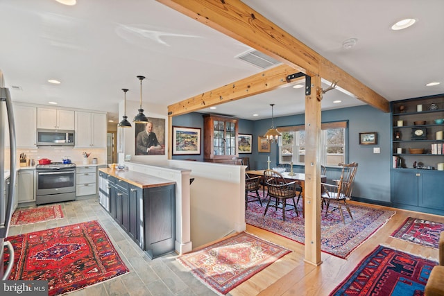 kitchen with light hardwood / wood-style flooring, beam ceiling, stainless steel appliances, white cabinets, and decorative light fixtures