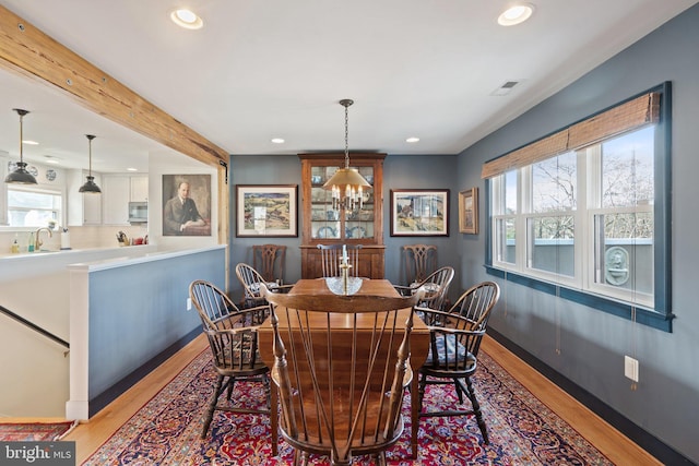 dining area with an inviting chandelier, beamed ceiling, sink, and light wood-type flooring