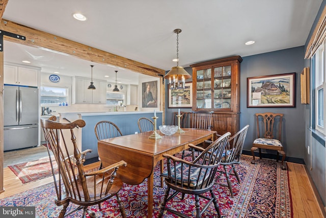 dining area with beamed ceiling, a chandelier, and light hardwood / wood-style flooring