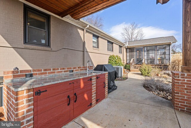 view of patio featuring cooling unit, sink, and a sunroom