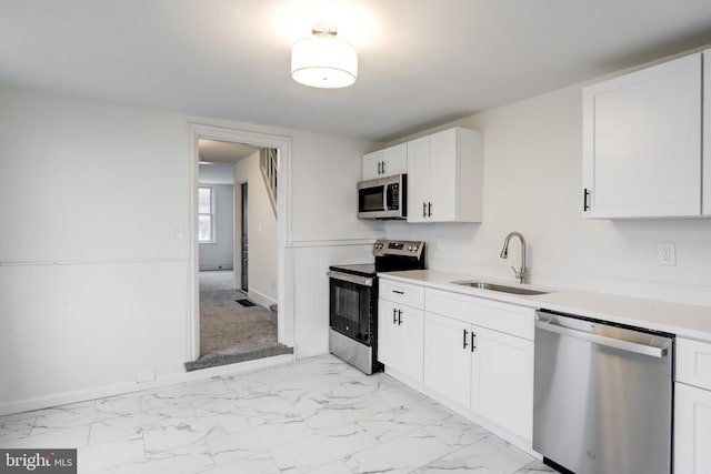 kitchen featuring marble finish floor, stainless steel appliances, a sink, and white cabinetry