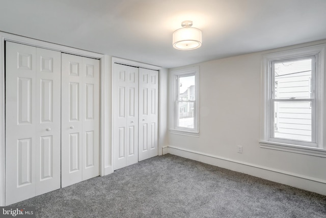 unfurnished bedroom with carpet flooring, baseboards, and two closets