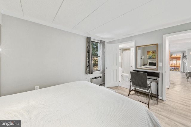 bedroom featuring ensuite bath, light hardwood / wood-style floors, and a wall unit AC