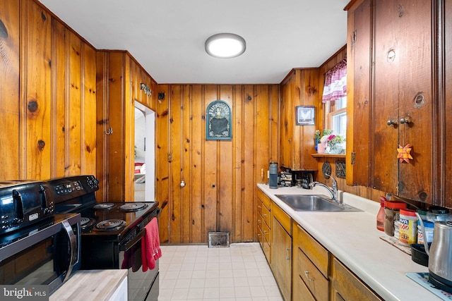 kitchen featuring wooden walls, brown cabinets, black electric range oven, light countertops, and a sink