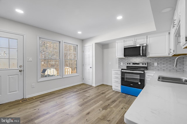 kitchen with sink, electric range oven, backsplash, light hardwood / wood-style floors, and white cabinets