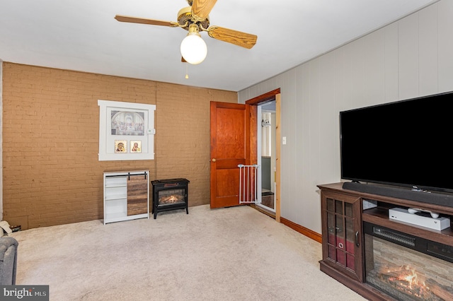 interior space with brick wall, a wood stove, light colored carpet, and ceiling fan