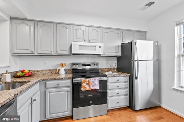 kitchen with light wood-type flooring, visible vents, stainless steel appliances, baseboards, and light stone countertops