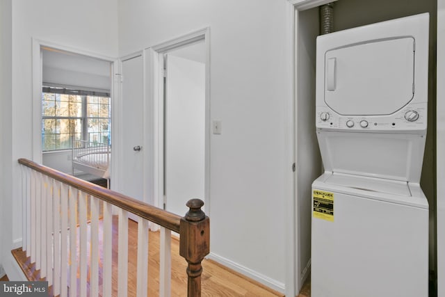 laundry room with light wood-type flooring, stacked washer / drying machine, baseboards, and laundry area