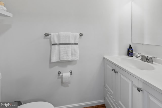 half bath featuring vanity, toilet, and baseboards