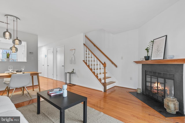 living room featuring a fireplace with flush hearth, stairway, baseboards, and wood finished floors