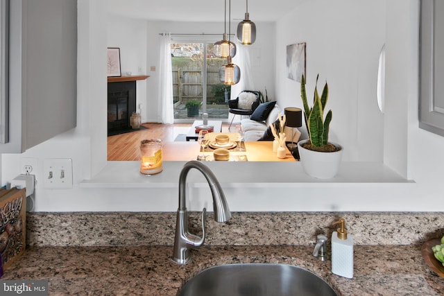 kitchen featuring decorative light fixtures, a fireplace with flush hearth, stone countertops, and a sink