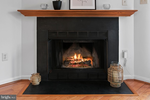 interior details featuring a fireplace with flush hearth, wood finished floors, and baseboards