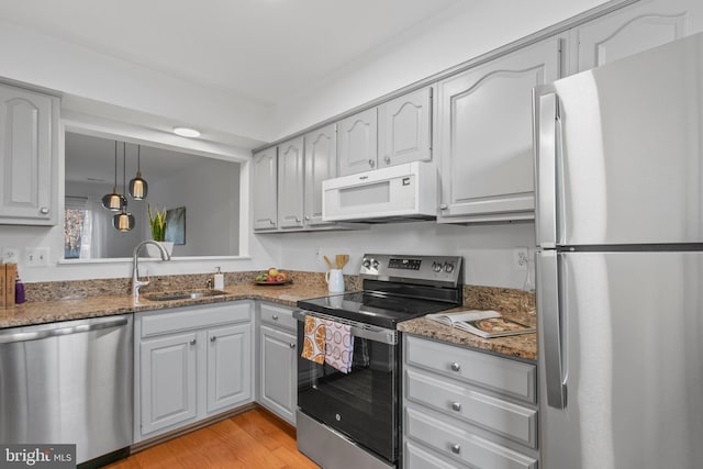 kitchen with light wood finished floors, stone counters, appliances with stainless steel finishes, hanging light fixtures, and a sink