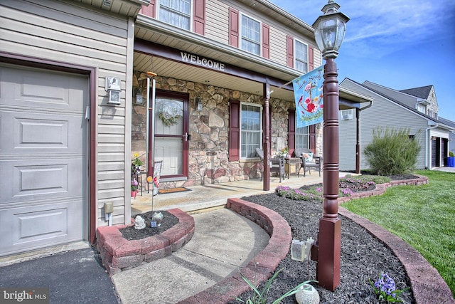 doorway to property with covered porch, a yard, stone siding, and a garage